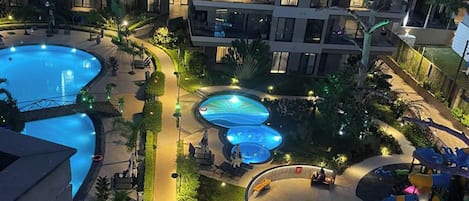 A multi-level hotel with a large outdoor swimming pool area, including a children's play area and multiple hot tubs.
