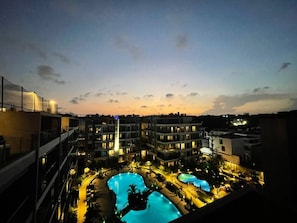 A hotel complex with multiple swimming pools, a central building with a flag, and surrounding balconies.