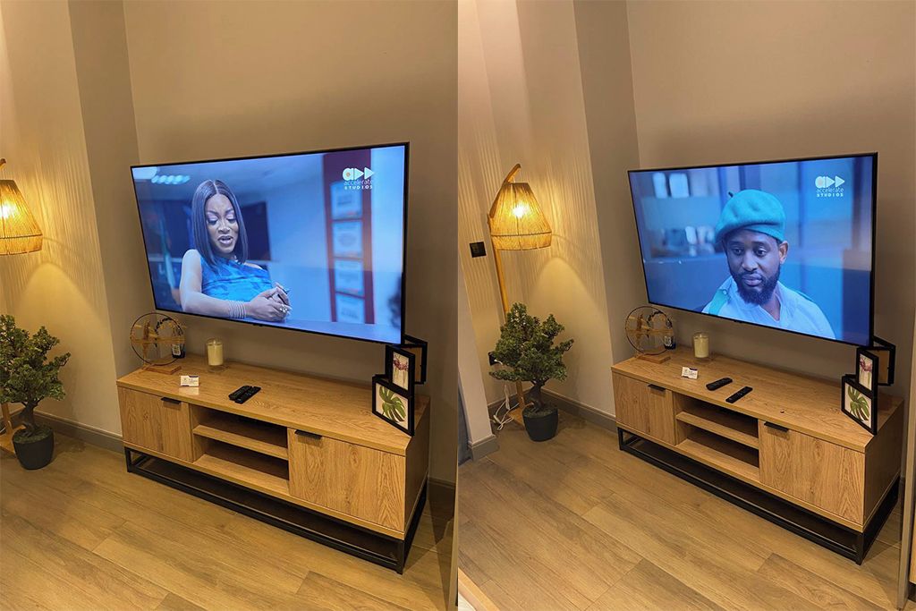 Two televisions mounted on wooden stands with remote controls, a small plant, and a lamp on each stand.