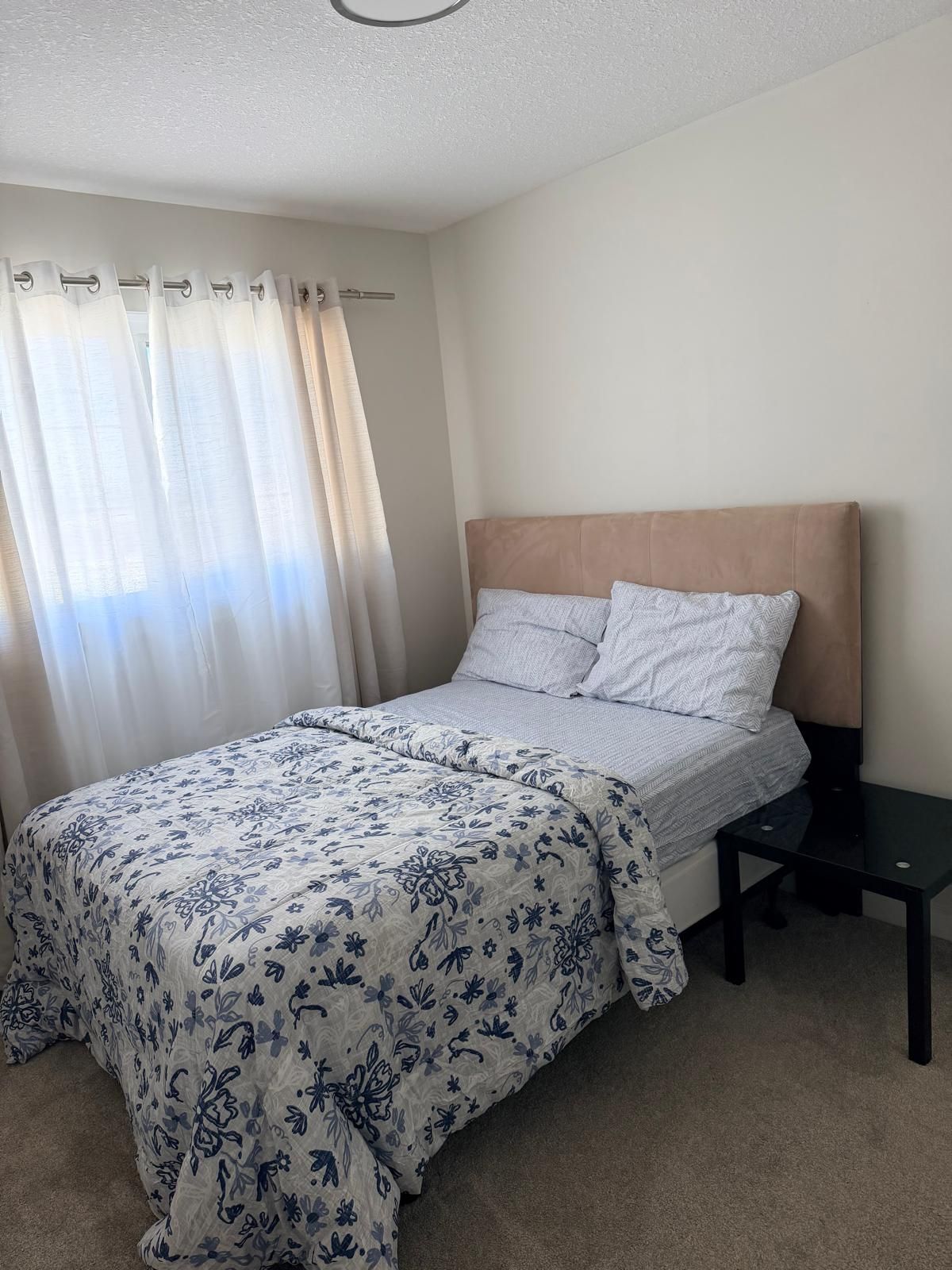 Een slaapkamer met een bed, nachtkastje en een raam met gordijnen.