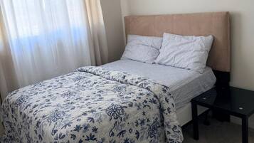 Een slaapkamer met een bed, nachtkastje en een raam met gordijnen.