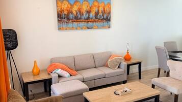 Een moderne woonkamer met een bank, fauteuils, een salontafel en een schilderij aan de muur.