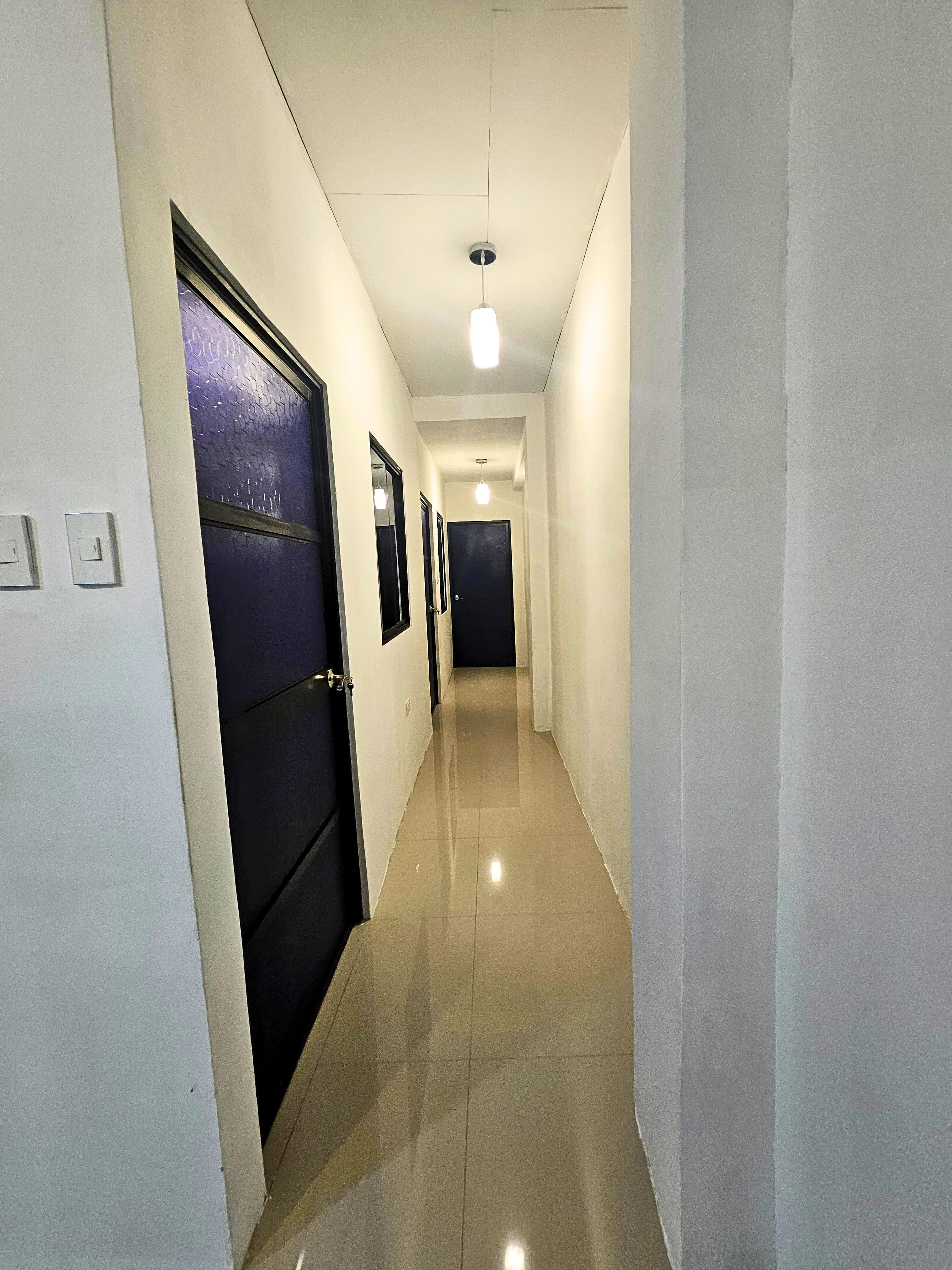 Un couloir avec des portes, des luminaires et un sol carrelé.