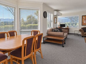 A living room with a dining table, chairs, a sofa, and a TV. - Kings Drive Family Retreat | 4BR Home, Sleeps 9 (Wānaka)