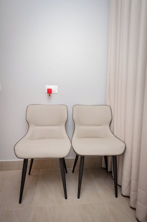 Two modern chairs with a unique design, positioned against a plain wall with a light switch and a curtain. - Hotel Melung (Kathmandu)