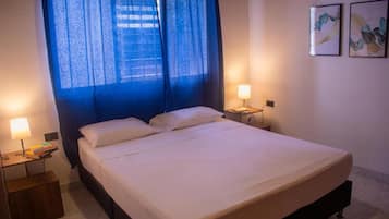 Habitación de hotel con una cama, dos mesitas de noche y un ventanal con cortinas.