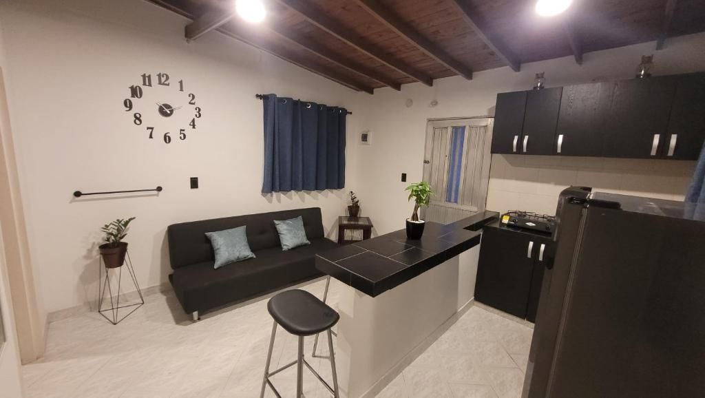 Un espacio habitable compacto con kitchenette, un sofá con cojines, un reloj en la pared y una planta en maceta.