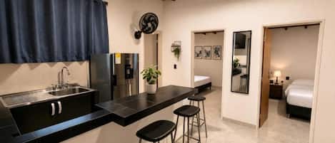 A modern kitchen with a black countertop, stainless steel appliances, and a bar stool area.