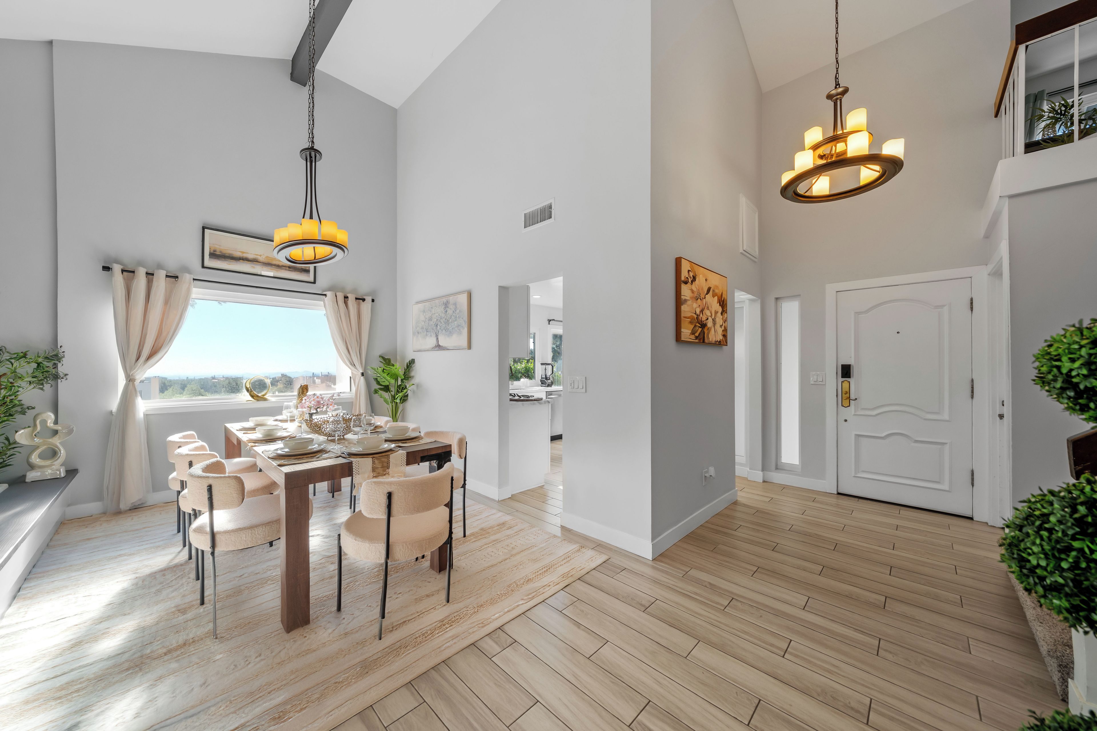 A spacious dining area with a wooden table and chairs, a chandelier, and a view through a window with curtains.