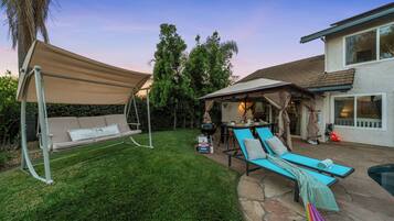 Un jardin avec une balançoire, un patio couvert, une piscine et une terrasse en pierre.