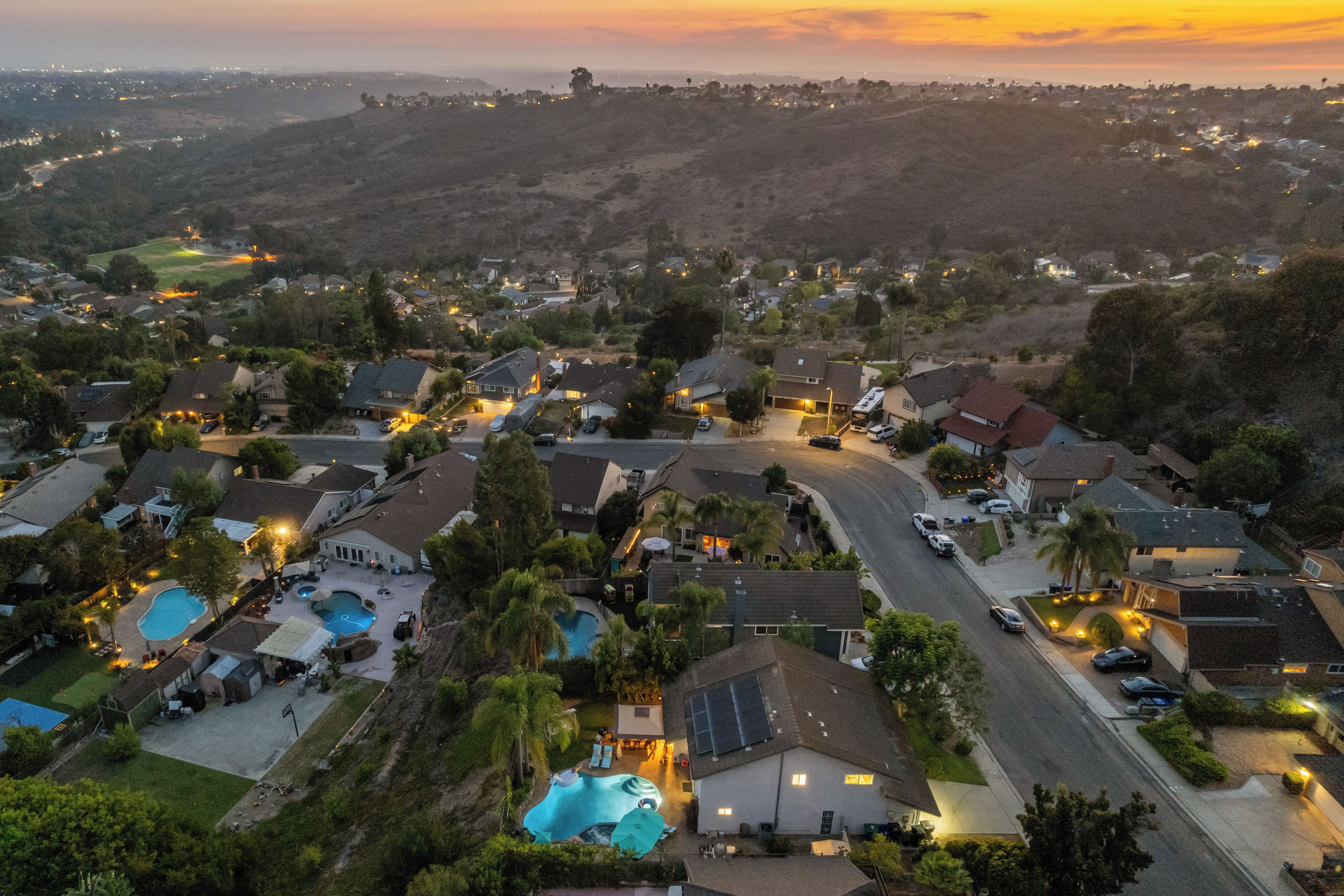 Un quartier résidentiel avec des maisons, une piscine et, au loin, un paysage vallonné.