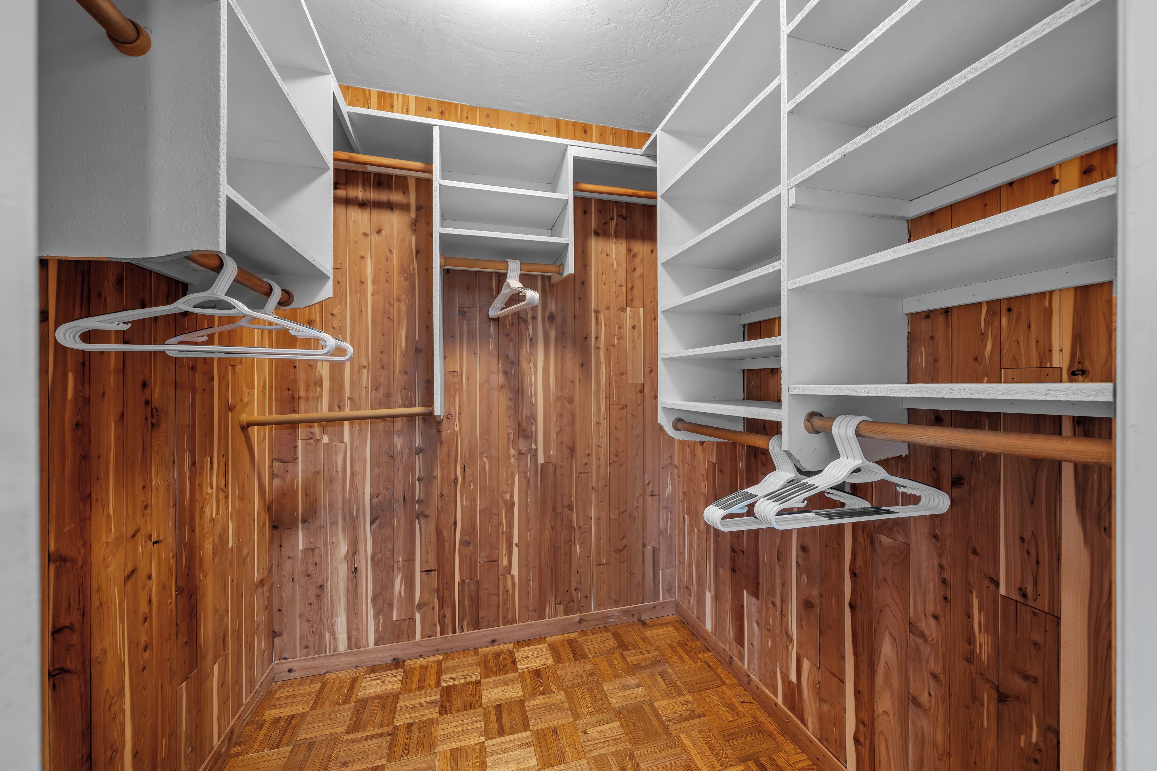 Ein begehbarer Kleiderschrank mit Holzboden, weißen Regalen und Holzvertäfelung.