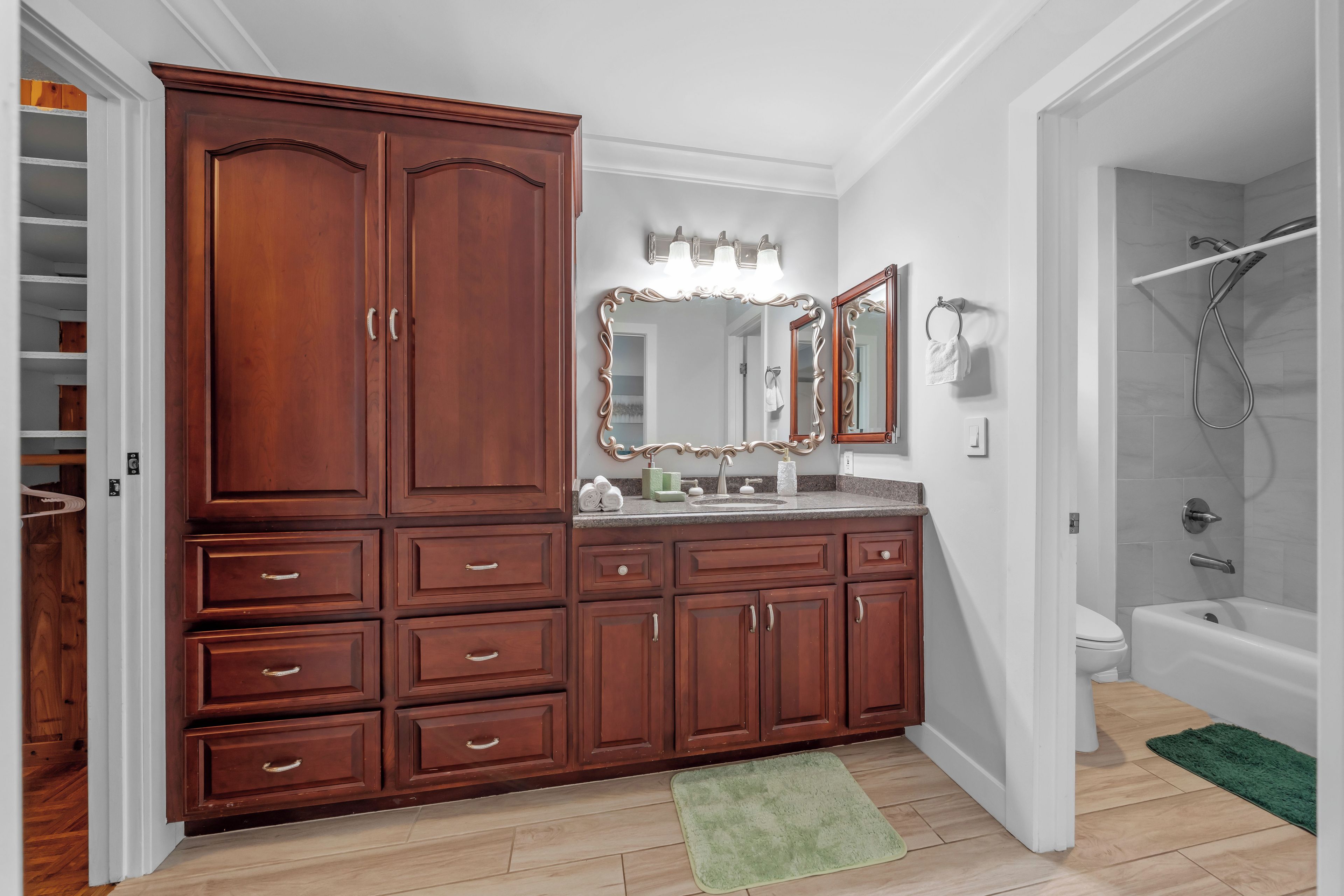 Une salle de bain avec un meuble-lavabo en bois, un grand miroir, une douche et un tapis vert.