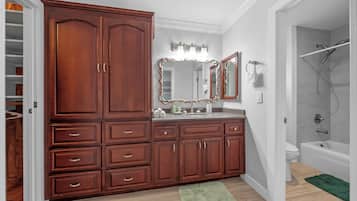 Een badkamer met een houten wastafelmeubel, een grote spiegel, een douche en een groene kleed.