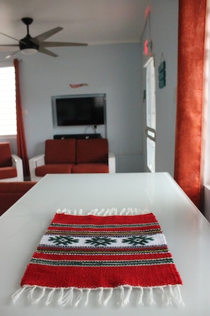 A living room with a white table, red sofa, and a television on the wall. - Casa Iliria 3: Fantastic Studio Within Walking Distance of Boqueron Beach (Boquerón)