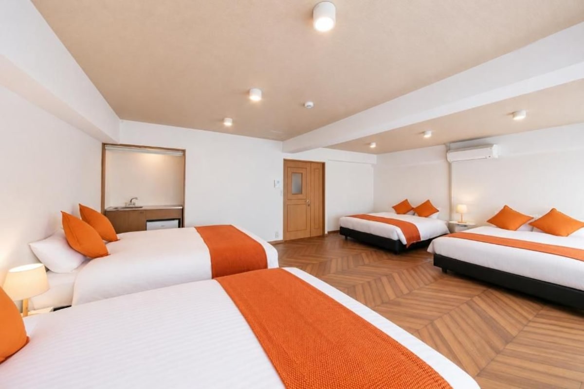 Habitació d'hotel amb tres llits, un sòl de fusta, un mirall i una porta.