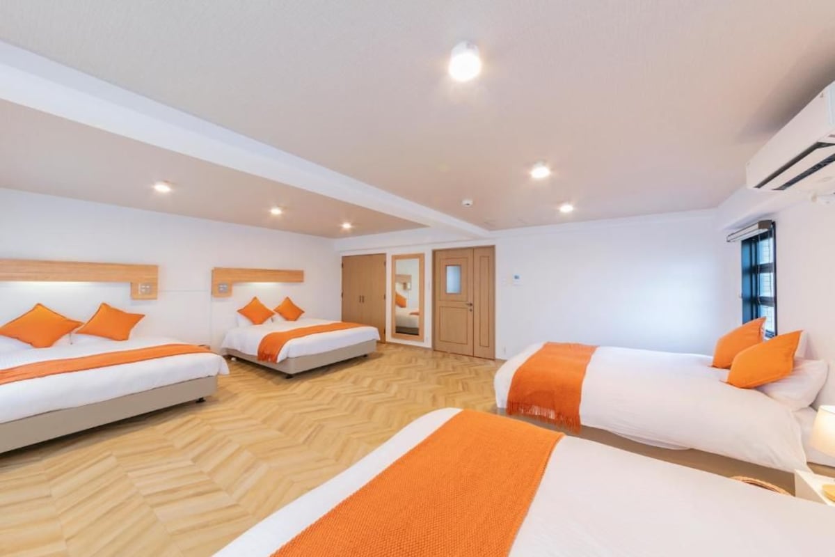 Habitació d'hotel amb tres llits, un terra de fusta i una porta que dona a una altra habitació.