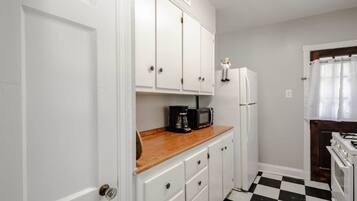 Una cocina compacta con armarios blancos, encimera de madera, cafetera negra, refrigerador blanco y piso a cuadros.