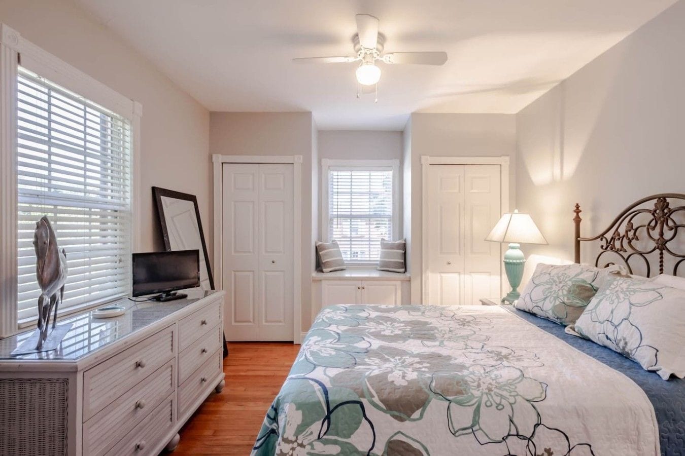 Un dormitorio con cama, cómoda, televisión y ventana con persianas.