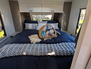 Een bed met een donkerblauwe dekbedovertrek, een gebreide plaid en een mandje met toiletartikelen.