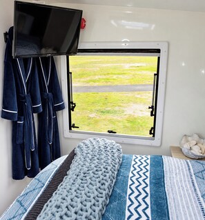 Een slaapkamer met een bed, een raam, een televisie en een handdoekenrek.