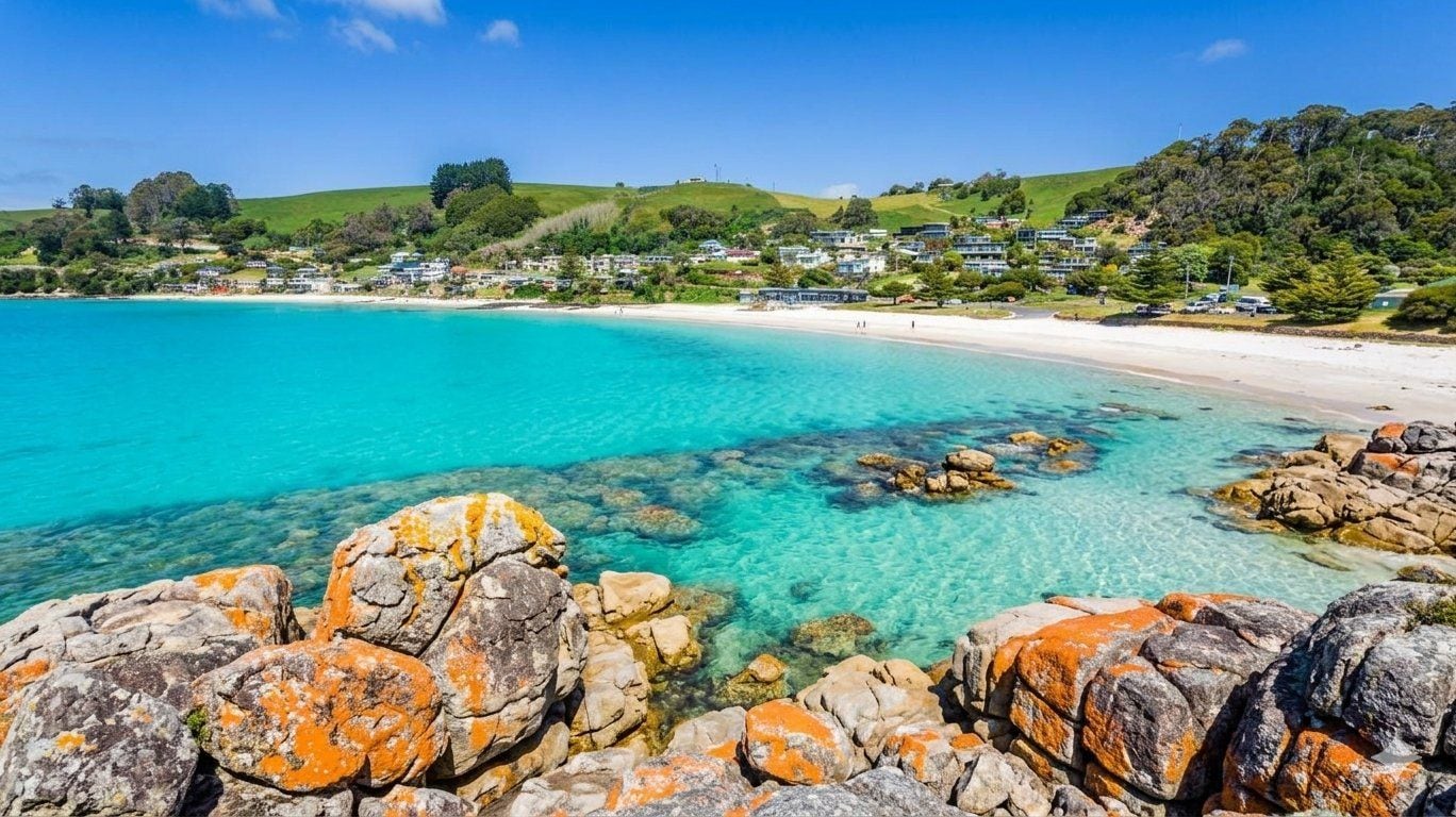 Paisagem costeira com águas turquesa cristalinas, afloramentos rochosos e uma praia arenosa.