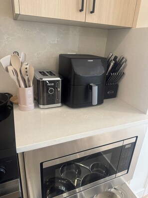A kitchen with a toaster, coffee maker, and utensils on the counter, and a microwave below. - Luxury Elegant Condo Prime Location & Parking (Calgary)