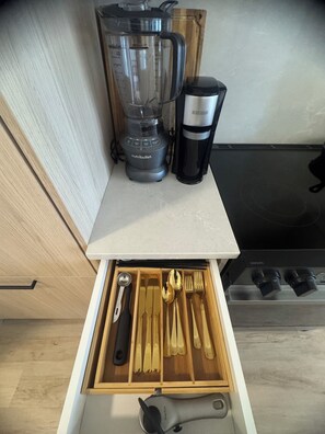 Eine Küchenarbeitsplatte mit einem Mixer, einer Kaffeemaschine und einer Schublade mit Besteck.