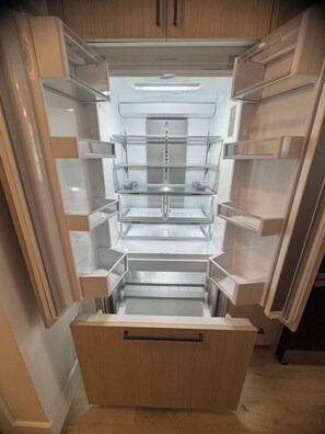 An open refrigerator with multiple shelves and a freezer compartment. - Luxury Elegant Condo Prime Location & Parking (Calgary)