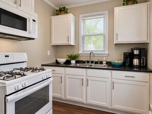 A kitchen with white cabinets, a stove, a microwave, a sink, and a window with blinds. - Charming 3 bedroom home near Galleria - Prime Location! (Minneapolis)