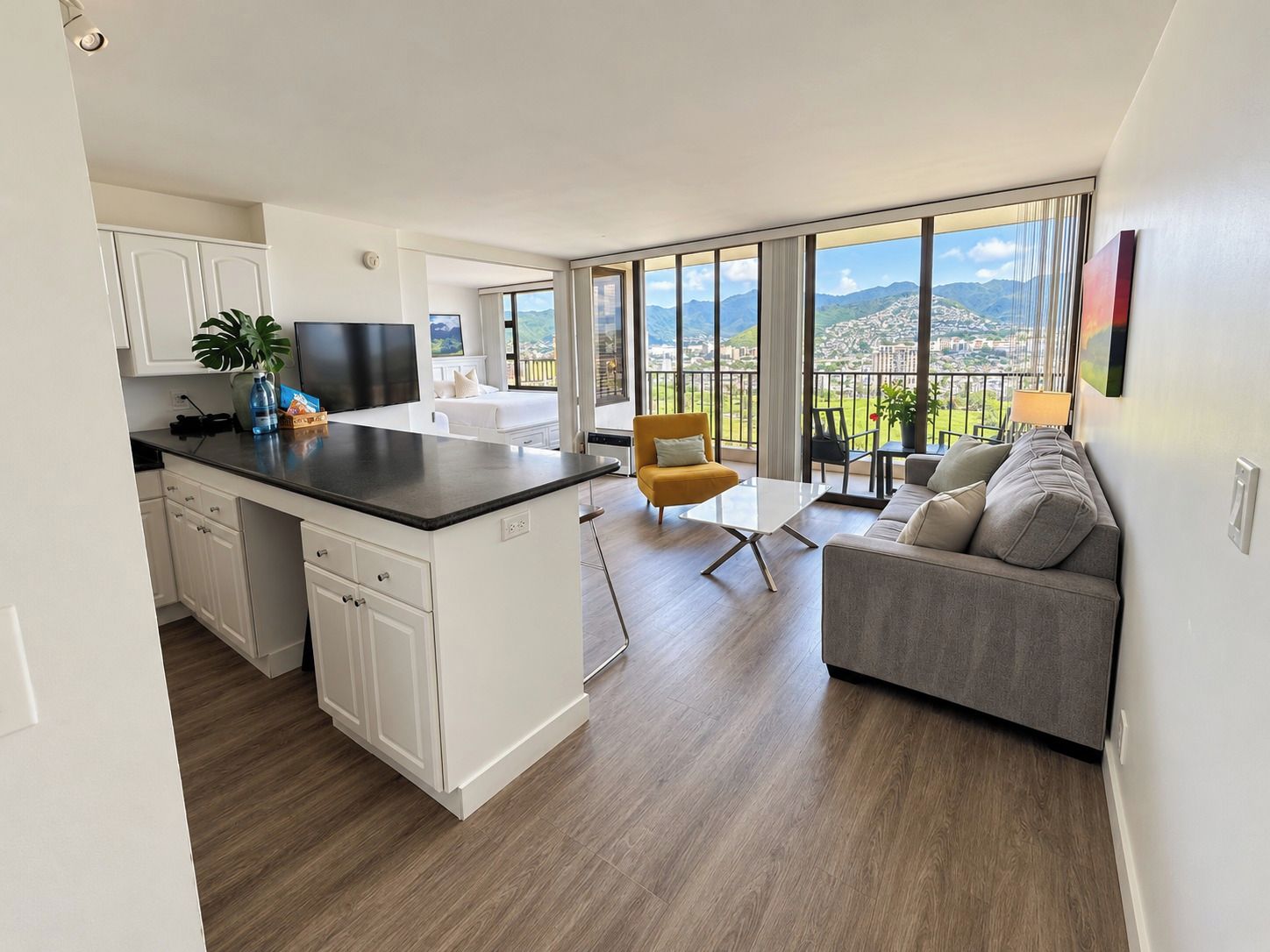 A modern apartment with a kitchen, dining area, and living room, featuring a large window with a mountain view.