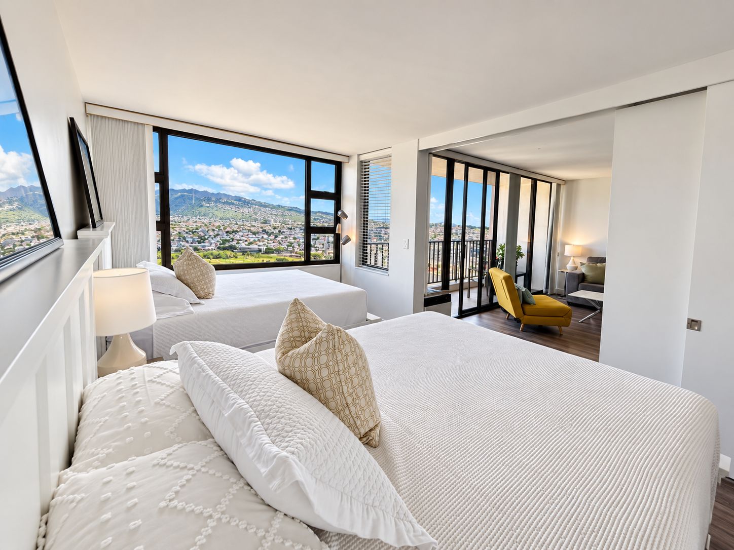 Ein Hotelzimmer mit zwei Betten, einem Balkon und Blick auf die Stadt sowie einem gelben Sessel.