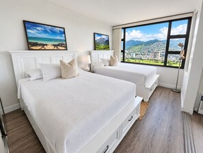 Quarto de hotel com duas camas, uma janela ampla com vista para a cidade e montanhas, e obras de arte na parede.