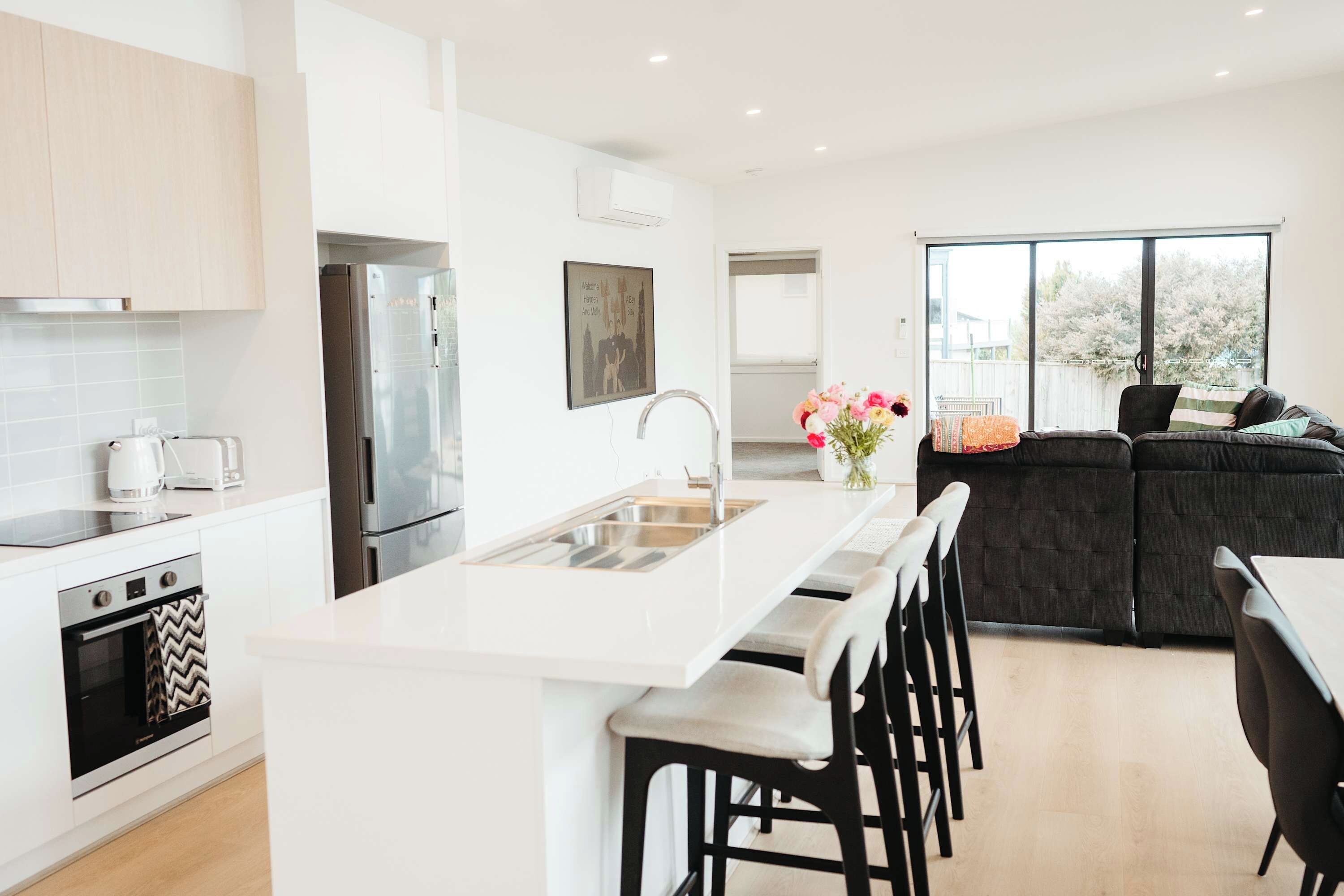 Una cocina moderna con una isla central, taburetes de bar, horno empotrado y un amplio ventanal.