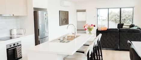 Una cocina moderna con una isla central, taburetes de bar, horno empotrado y un amplio ventanal.