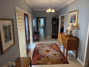Un couloir avec un banc en bois, un tapis à motifs floraux, une lampe et une horloge.