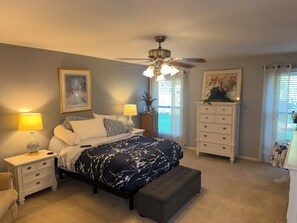 Une chambre à coucher comprenant un lit, des tables de chevet, une commode, un ventilateur de plafond et une fenêtre avec des rideaux.