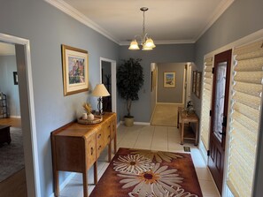 Un couloir avec une console en bois, une lampe, des œuvres d’art encadrées, une plante en pot et un tapis décoratif.