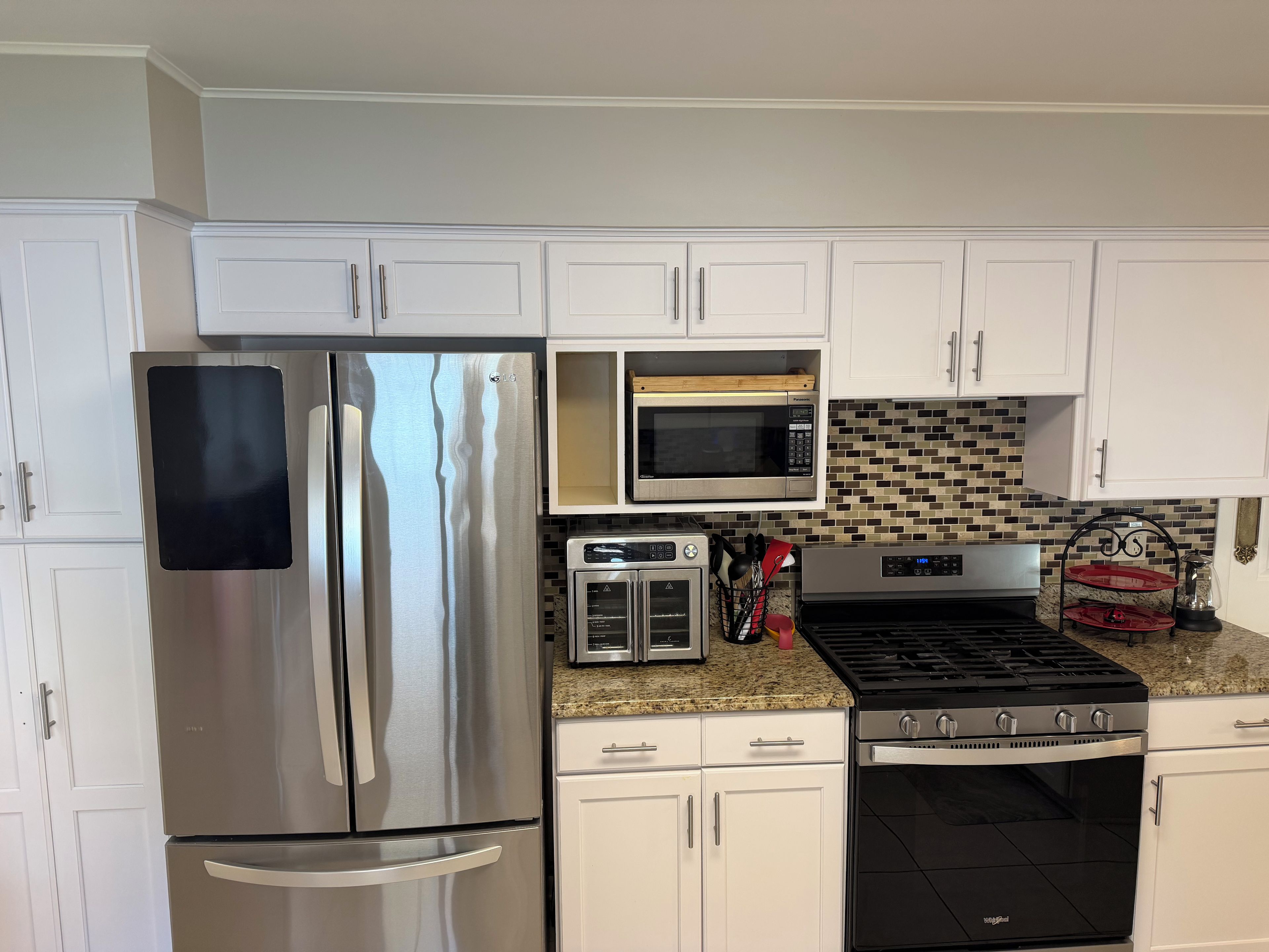 A kitchen with white cabinets, a stainless steel refrigerator, a microwave, a toaster, and a stove.