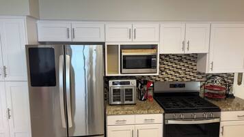 A kitchen with white cabinets, a stainless steel refrigerator, a microwave, a toaster, and a stove.