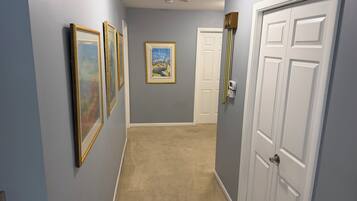 A hallway with light blue walls, a beige carpet, and white doors. There are framed pictures on the wall.