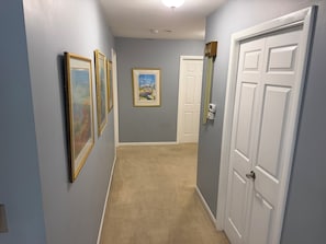 Un couloir aux murs bleu clair, avec un tapis beige et des portes blanches. Des tableaux encadrés ornent le mur.