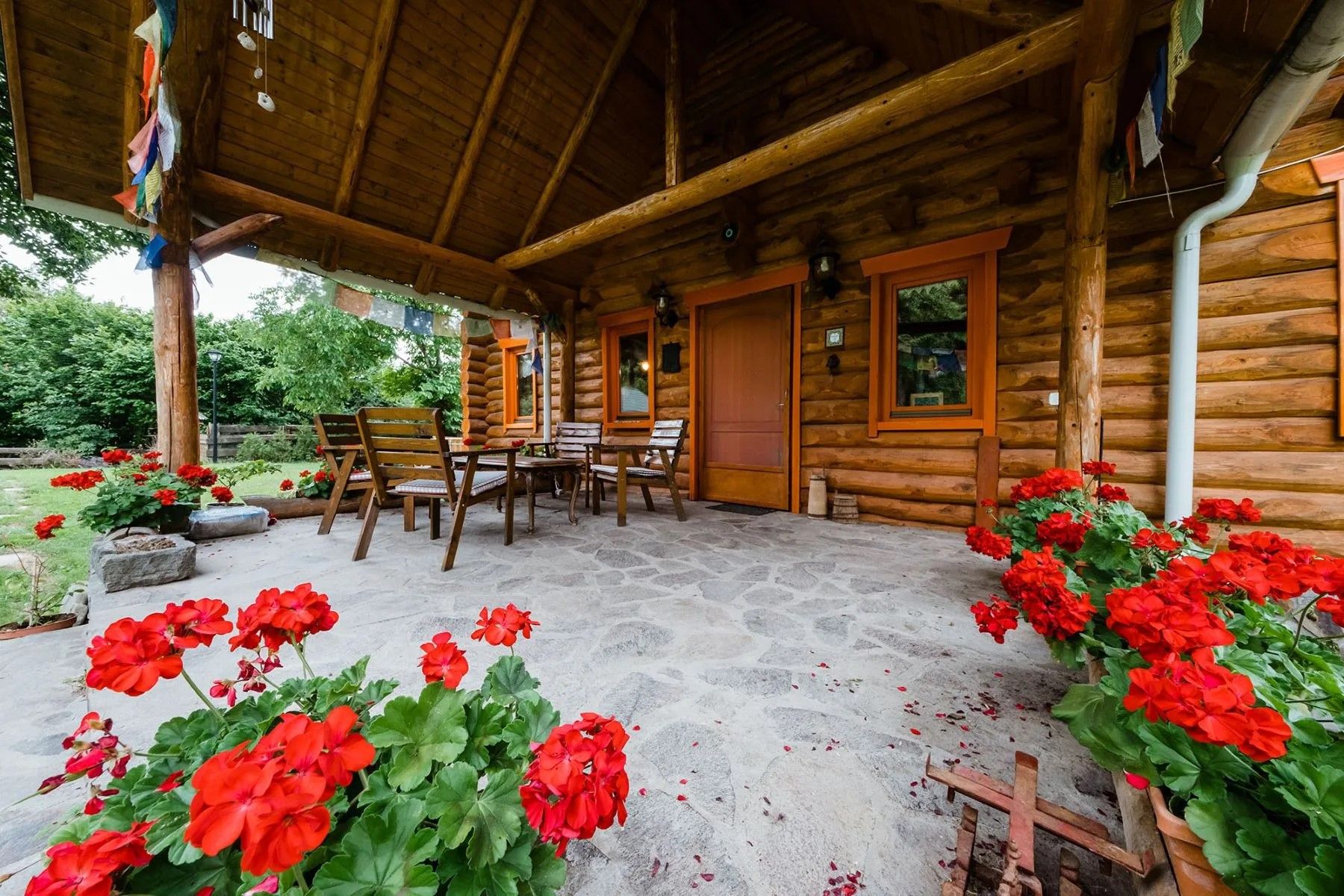 Une cabane en bois avec un porche, un sol en pierre et des fleurs rouges.