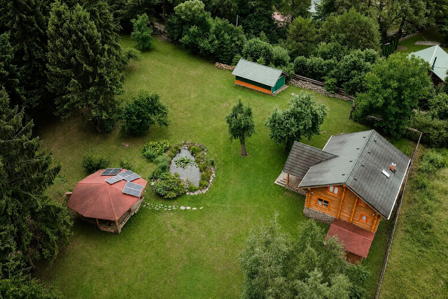 Vue aérienne d’une propriété comprenant une grande maison en bois, un petit abri et un étang bordé d’une structure circulaire en pierre.
