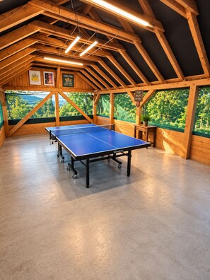 An indoor ping pong table with a ceiling of wooden beams and a view of greenery outside.