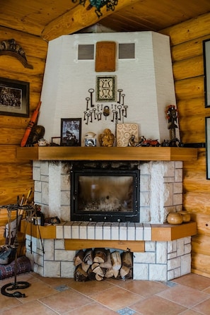A fireplace with a stone surround, a mantel decorated with various items, and a log storage area below. - Traditional Wooden Cottage with private garden situated in Campu Cetatii (Câmpu Cetăţii)