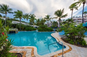 Ein Pool mit Steinrand, umgeben von Palmen und einem Gebäude im Hintergrund.