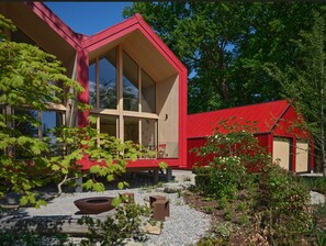 A modern house with a red exterior, large windows, and a patio area with outdoor furniture. - Seeberg Homes - House 2 (Schondorf am Ammersee)