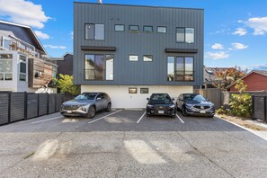 A modern building with a grey facade, three parking spaces, and two parked SUVs. - Brand New!~Lux~Skyline Views~4 bedrooms (Seattle)