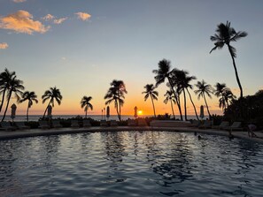 Zona de piscina con sillas de descanso y palmeras al atardecer.